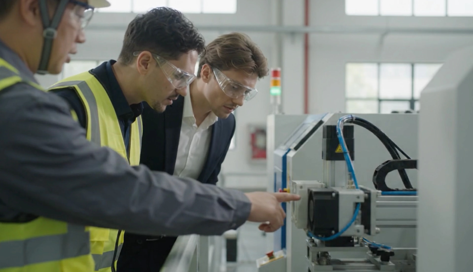 Three specialists in high-visibility vests inspecting automated machinery on a factory floor